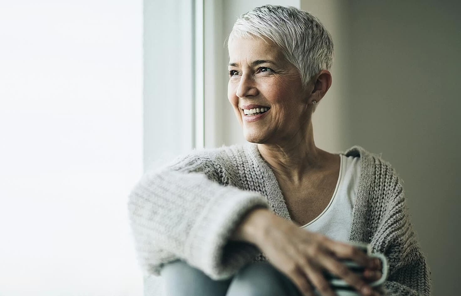 Smiling older woman sitting by a window.