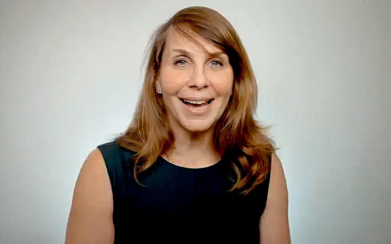 Woman gesturing while speaking against a neutral background.