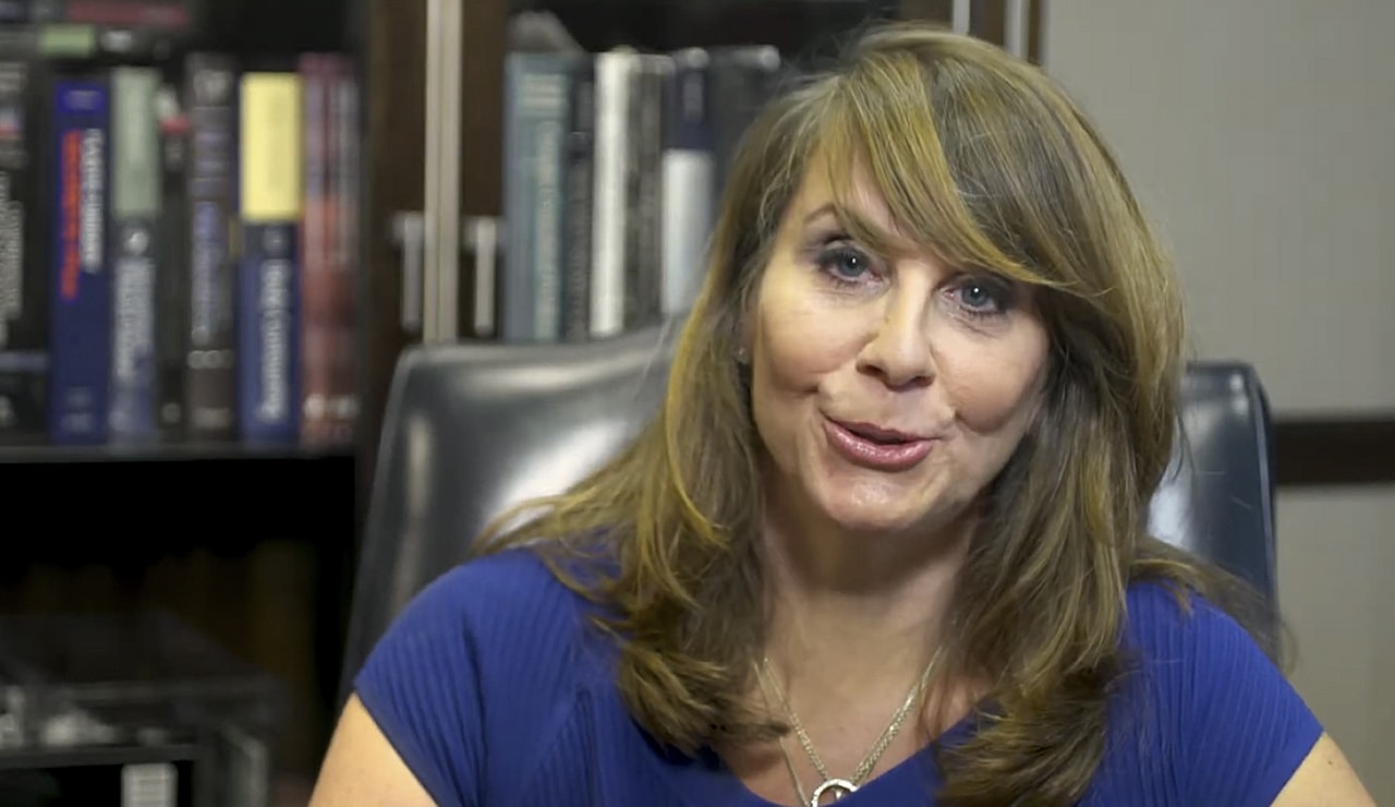Person speaking in front of a bookshelf.